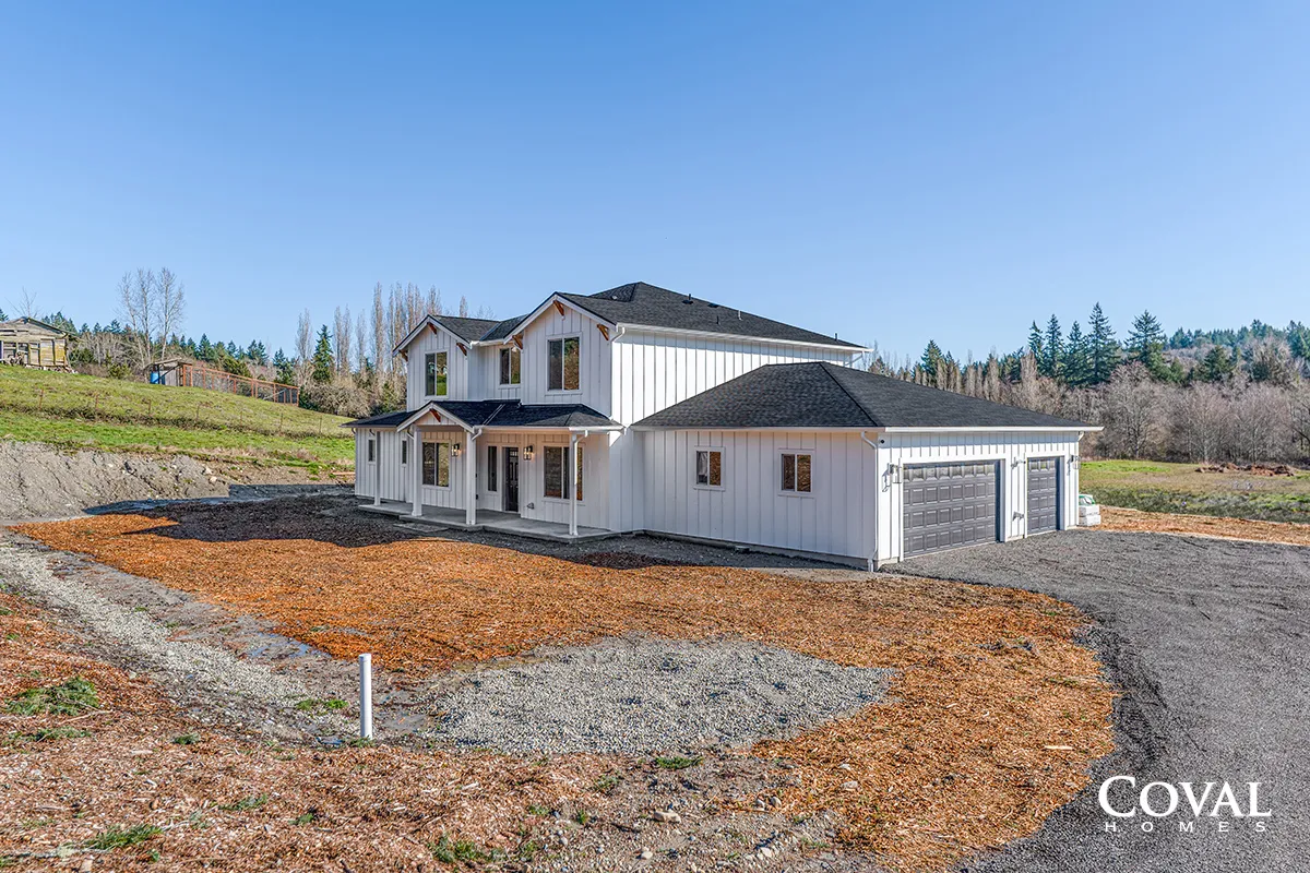 Newly built white two-story house with garage on a bare lot under a clear blue sky