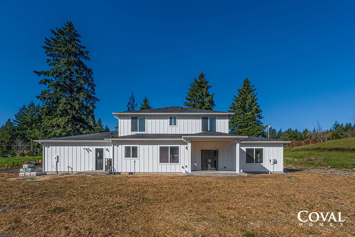 White two-story house with a covered porch on a grassy lot under a clear blue sky