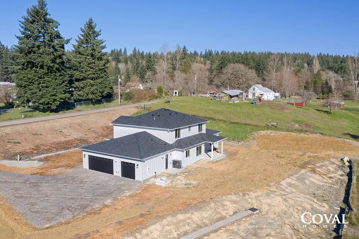 Aerial view of a gray house under construction on a large rural lot with trees and neighboring homes.