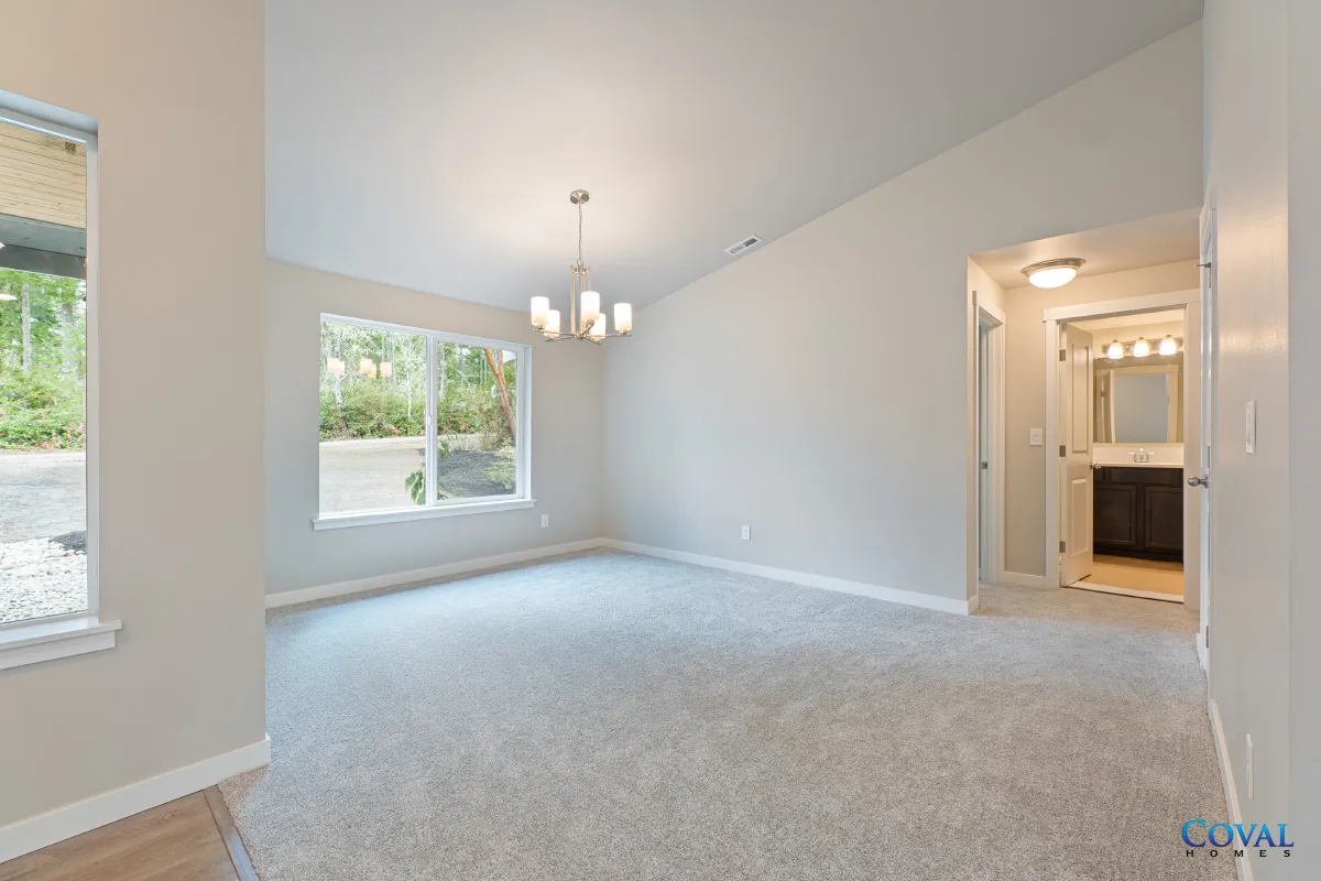 Empty carpeted living room with large windows, white walls, and adjoining bathroom vanity area