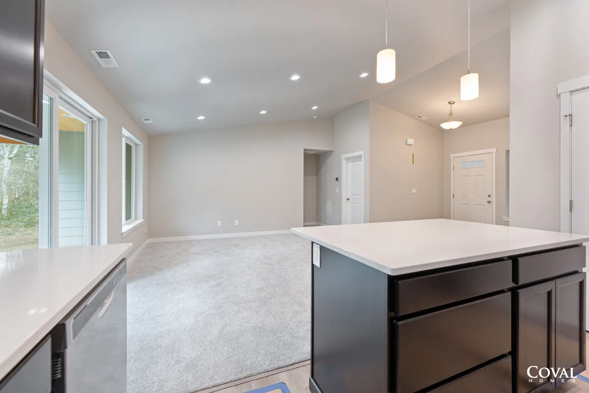 Bright empty open-plan living space with carpet, kitchen island, recessed lights, and large windows.