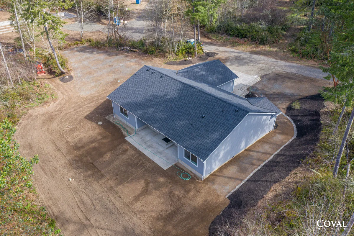 Aerial view of a gray-roofed house on a cleared wooded lot with dirt driveways.