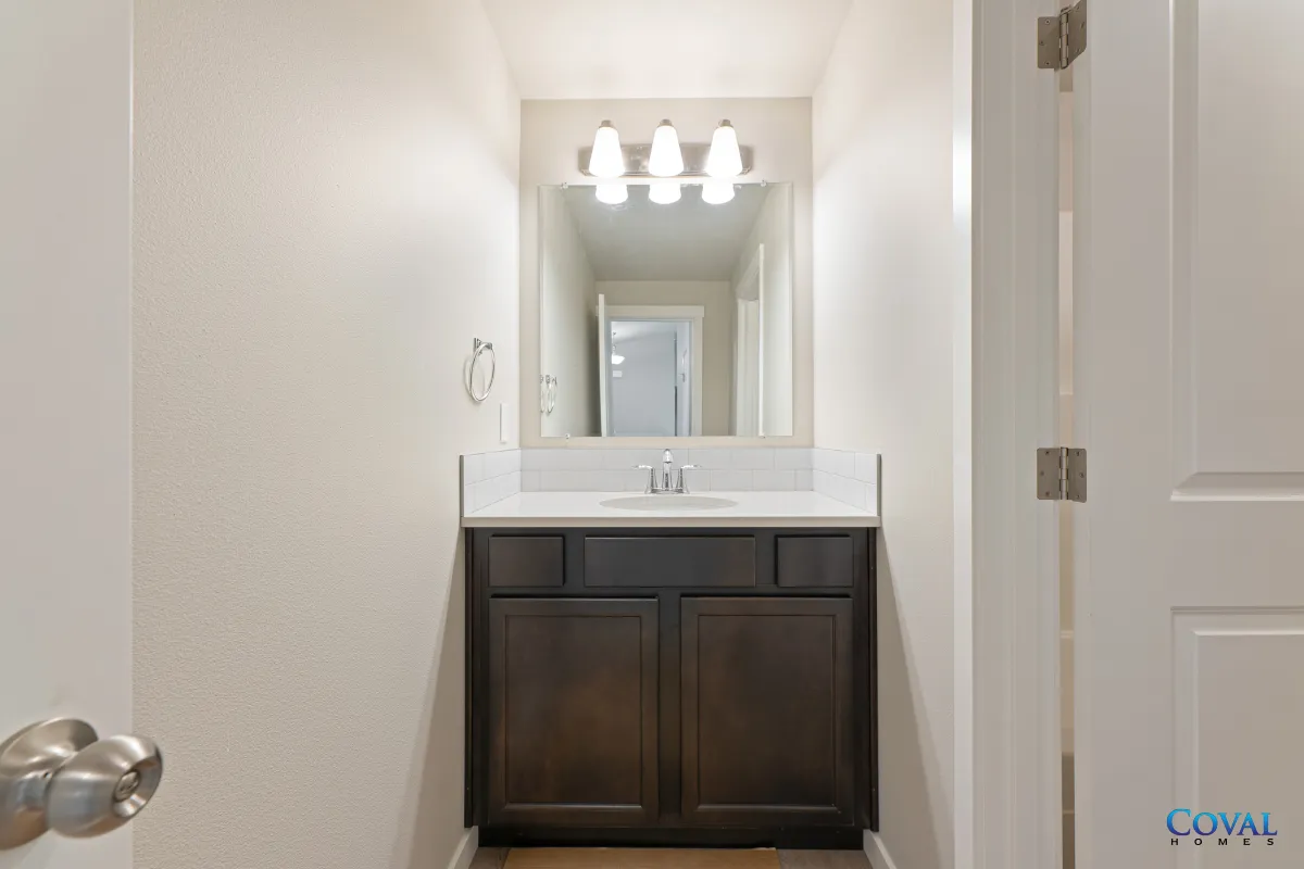 Narrow bathroom with dark vanity, white sink, and mirror under bright lights.