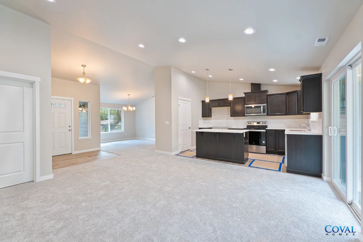 Open-concept living room and kitchen with gray carpet, white walls, and dark cabinets