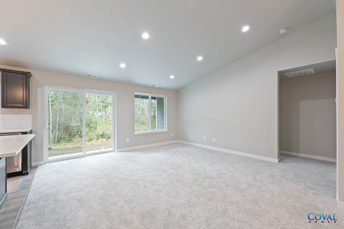 Empty carpeted living room with recessed lights, large windows, and a doorway to a hall