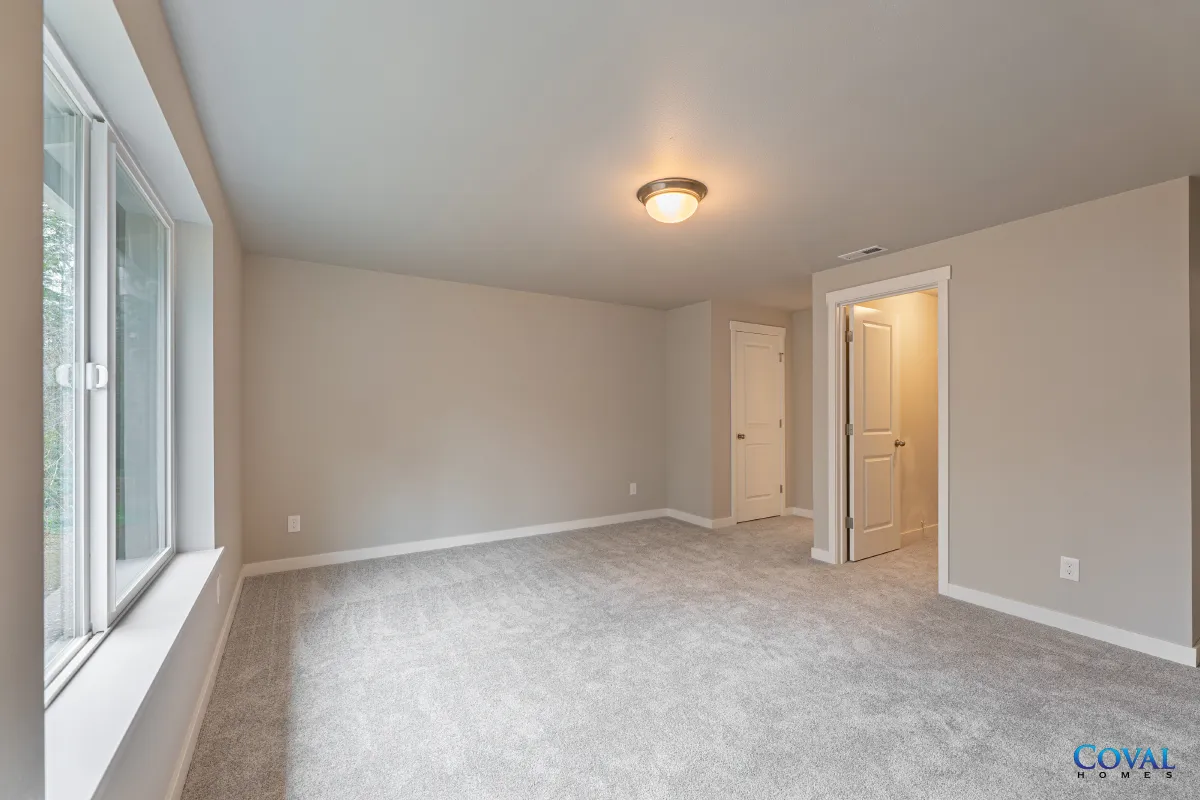 Empty carpeted bedroom with beige walls, large window, closet, and ceiling light
