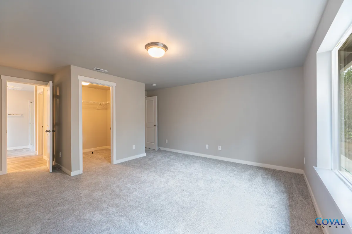 Empty gray bedroom with carpet, ceiling light, open doorway, and a large window.