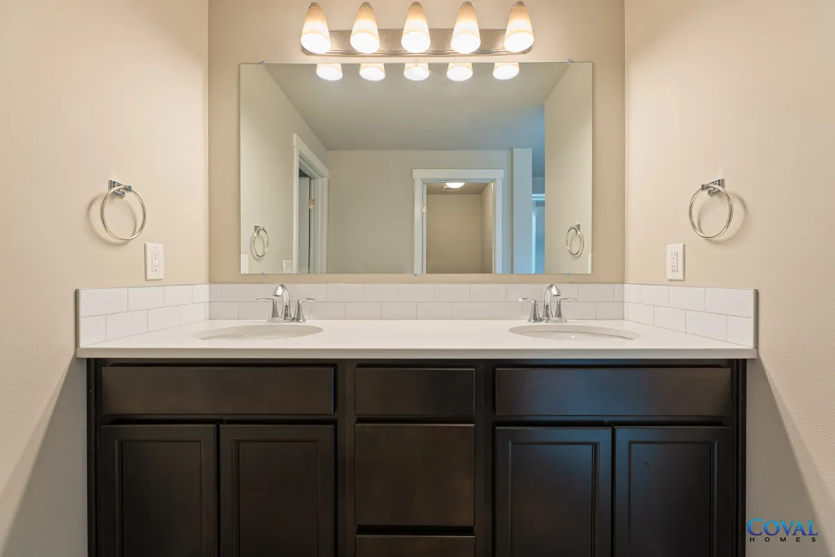 Modern bathroom vanity with double sinks, large mirror, and dark wood cabinets under bright lights
