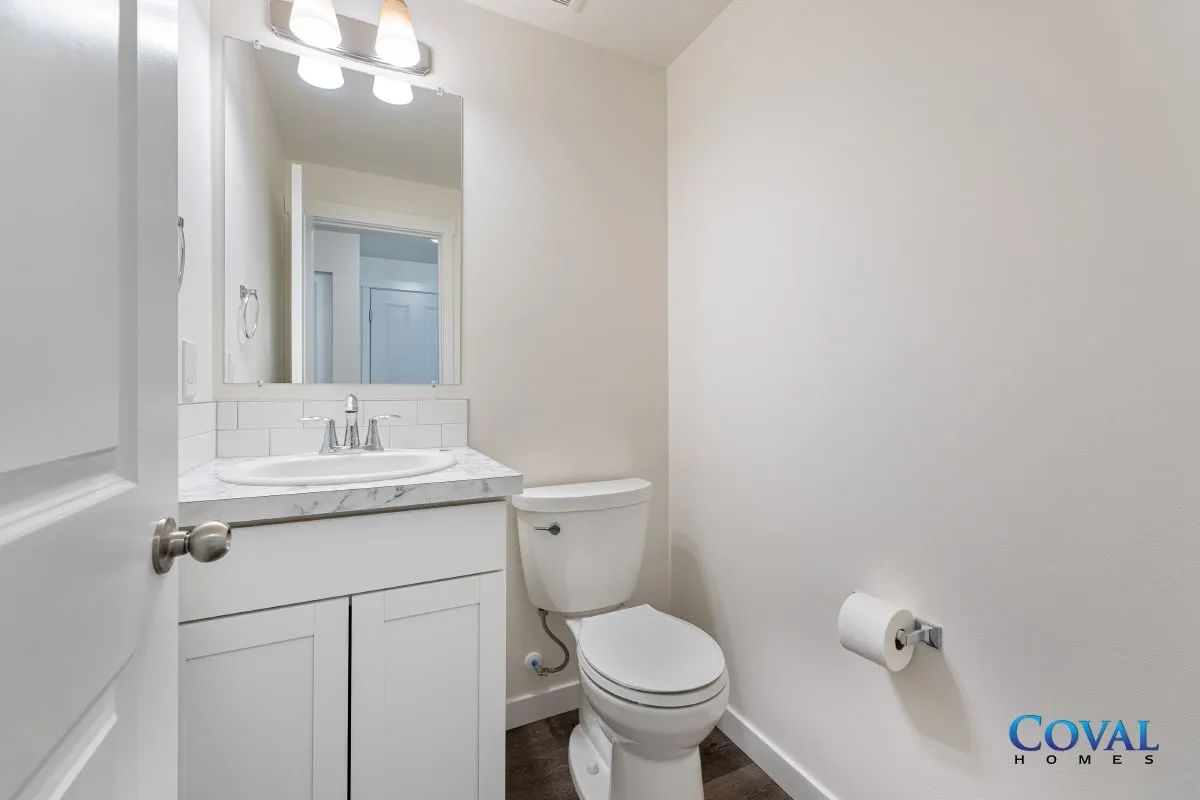 Small white bathroom with vanity, toilet, mirror, and towel holder