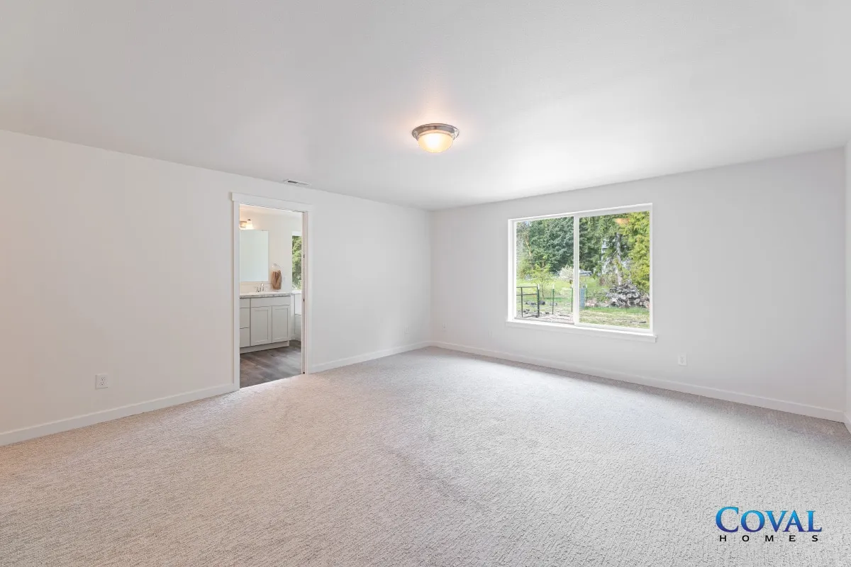 Empty carpeted room with white walls, a window, and an open doorway to a bathroom.