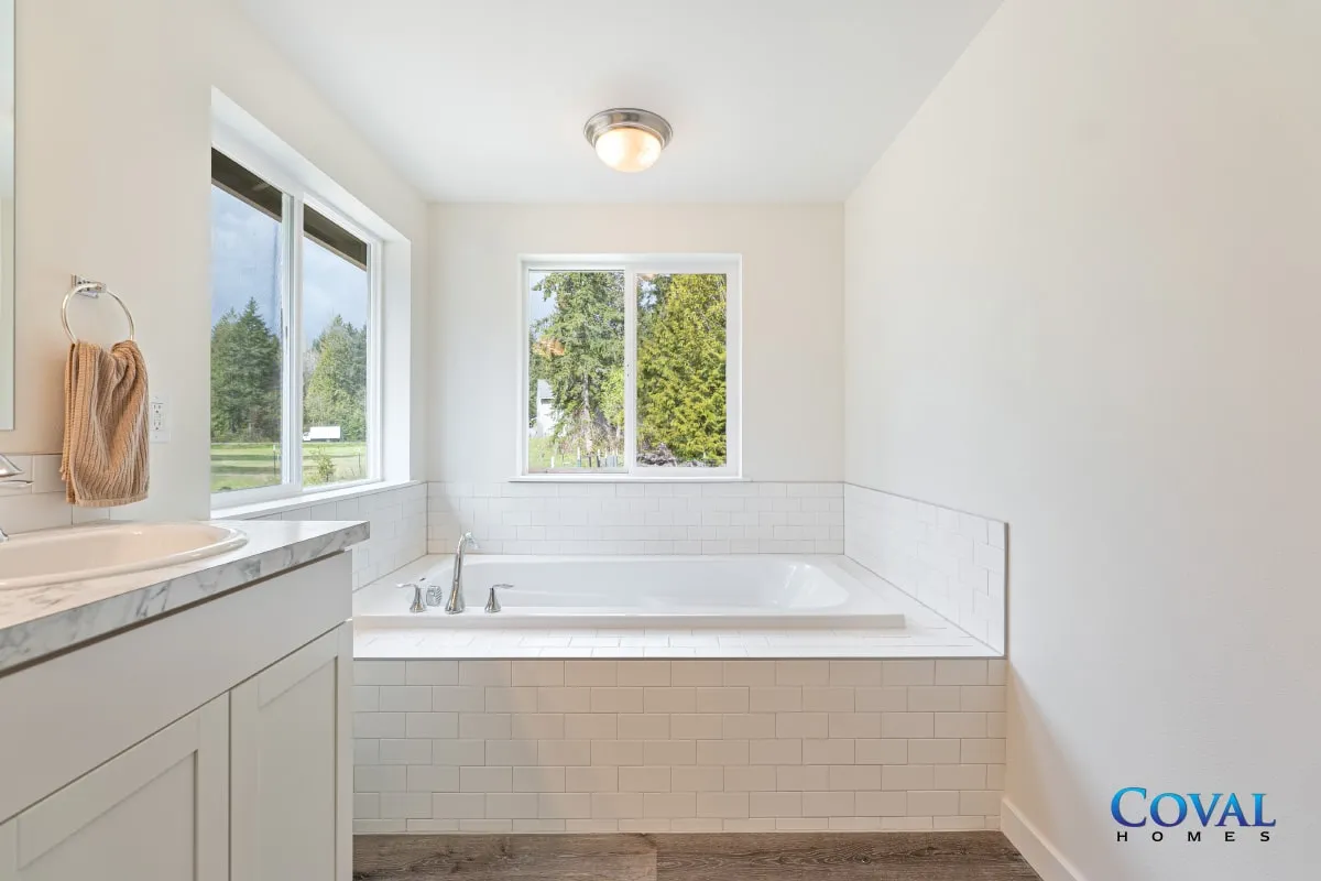 Bright white bathroom with a large soaking tub and windows overlooking greenery.