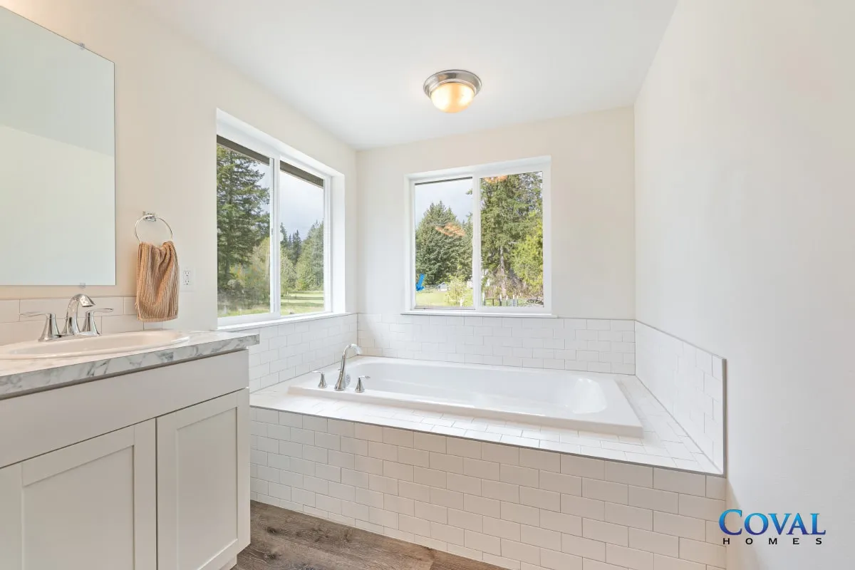 Bright white bathroom with a large soaking tub, vanity sink, and two sunlit windows