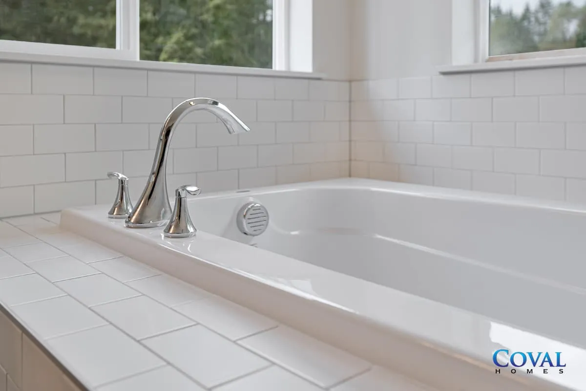 Bright white bathroom with a chrome faucet beside a soaking tub and tiled countertop.