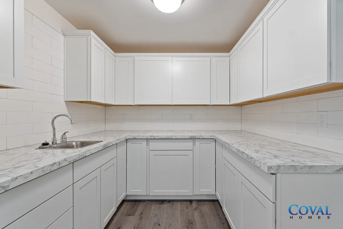 White U-shaped kitchen with marble counters, white cabinets, and wood flooring