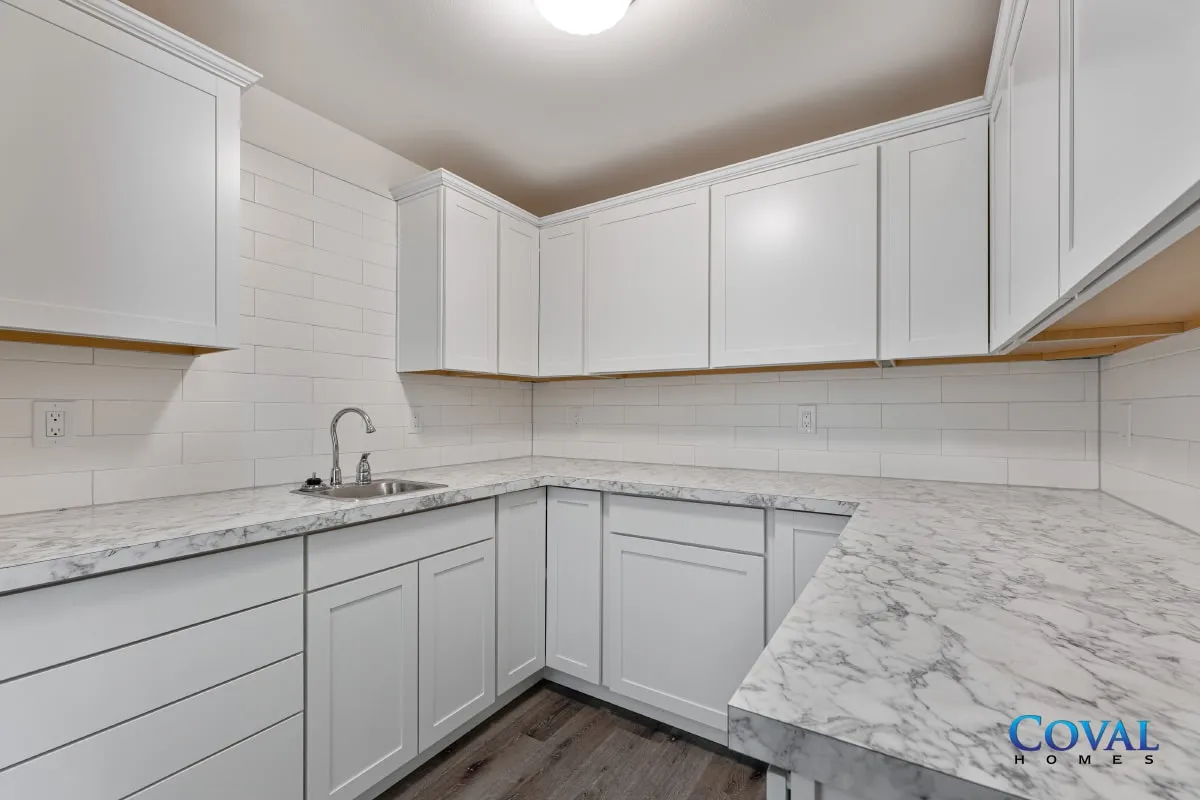 Bright white kitchen with marble countertops, white cabinets, and a stainless sink in an L-shaped layout