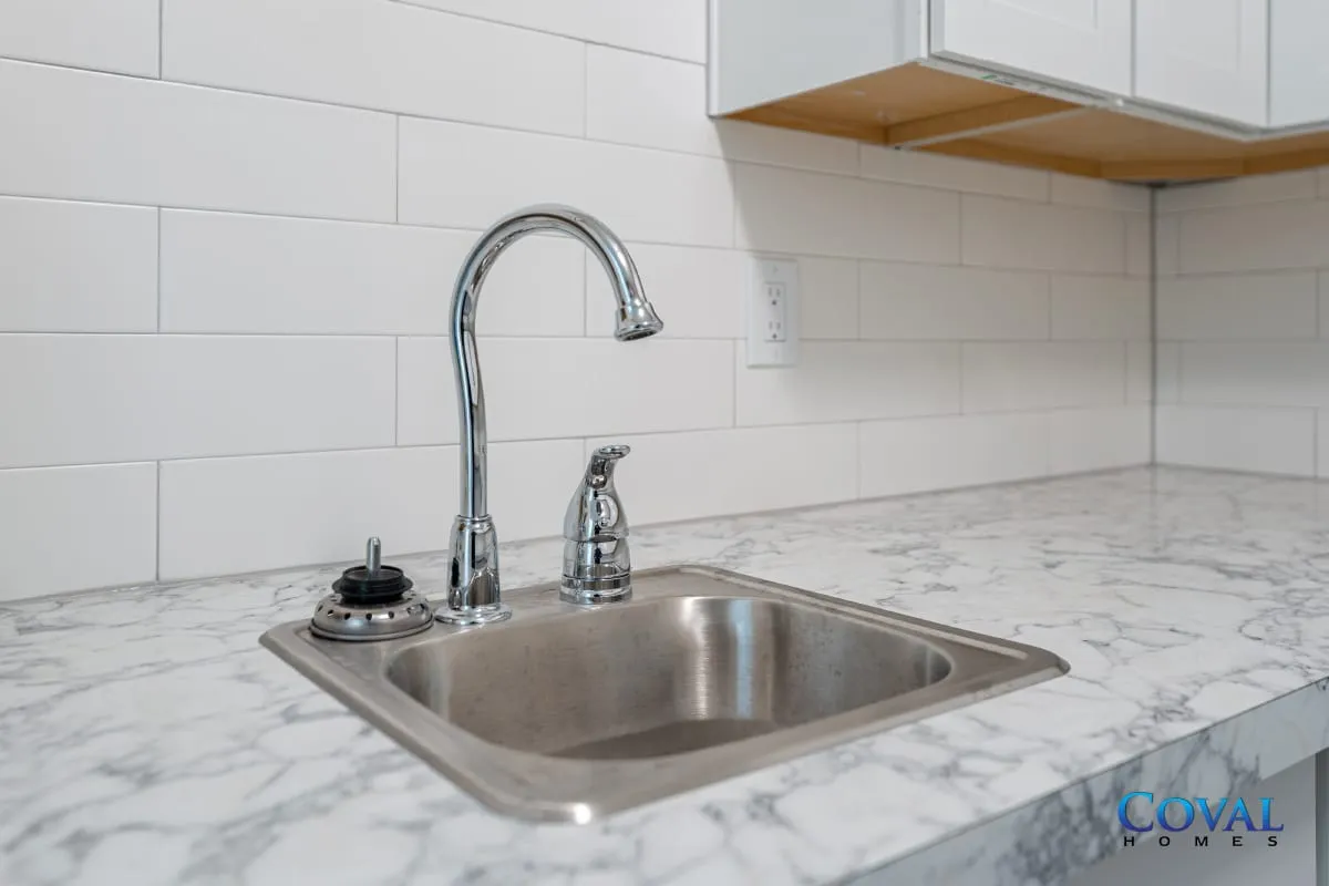 Kitchen sink with chrome faucet, marble countertop, white tile backsplash, and wood cabinets