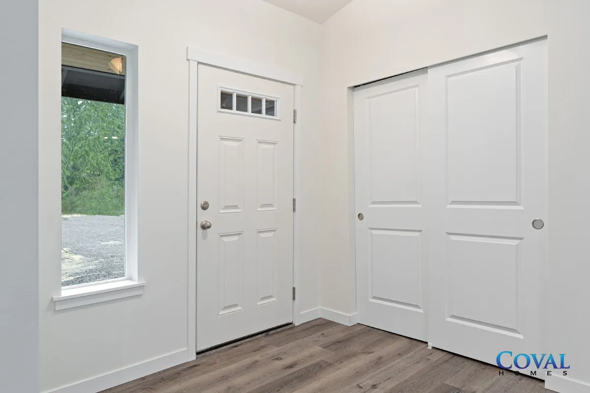 Bright empty bedroom with white walls, wood floor, window, and closet doors
