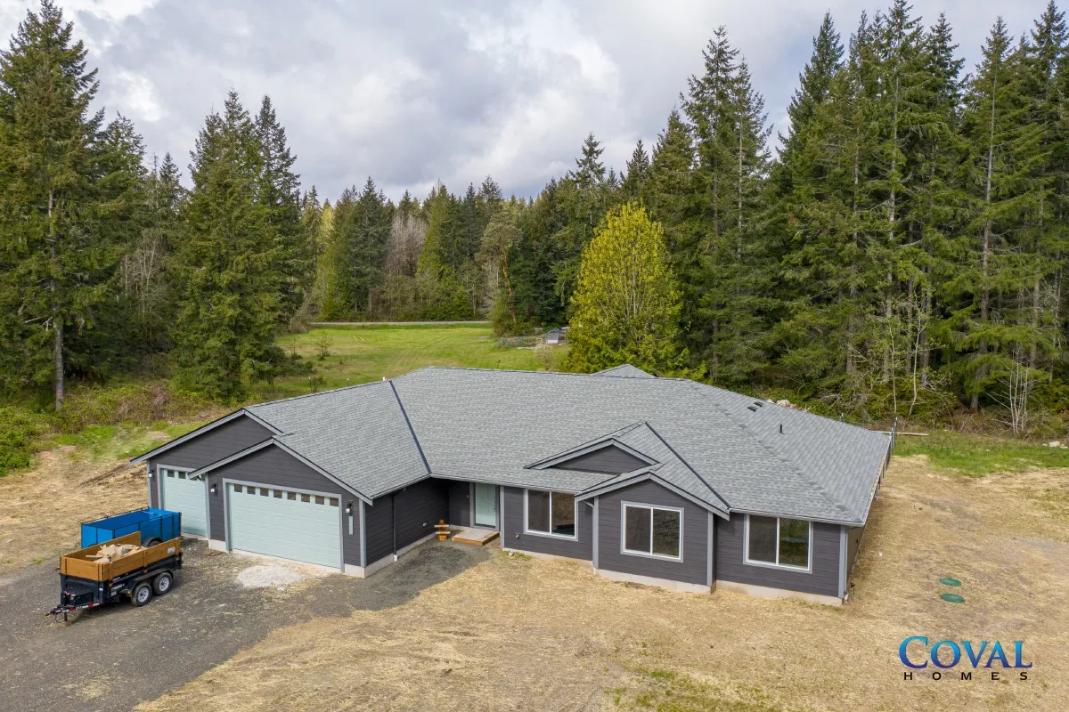 Aerial view of a gray house with a garage surrounded by trees in a wooded rural setting