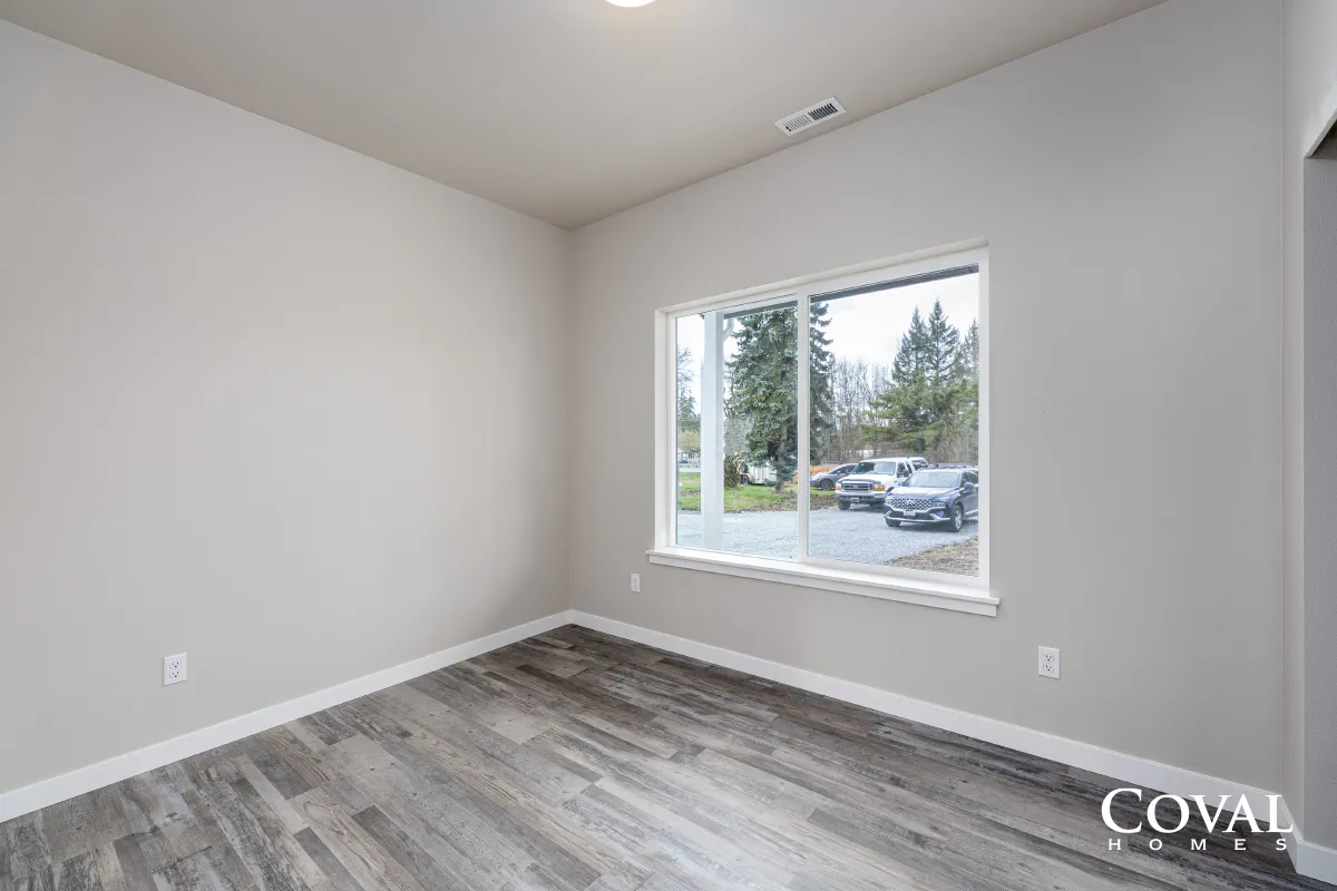 Empty modern bedroom with gray floors, white walls, and a large window overlooking trees and parked cars
