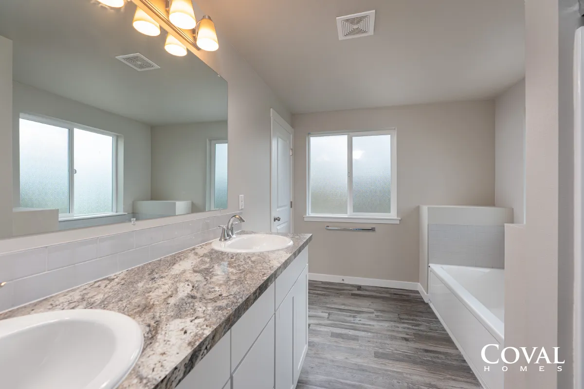 Bright modern bathroom with double vanity, granite countertop, large mirror, and soaking tub under a window