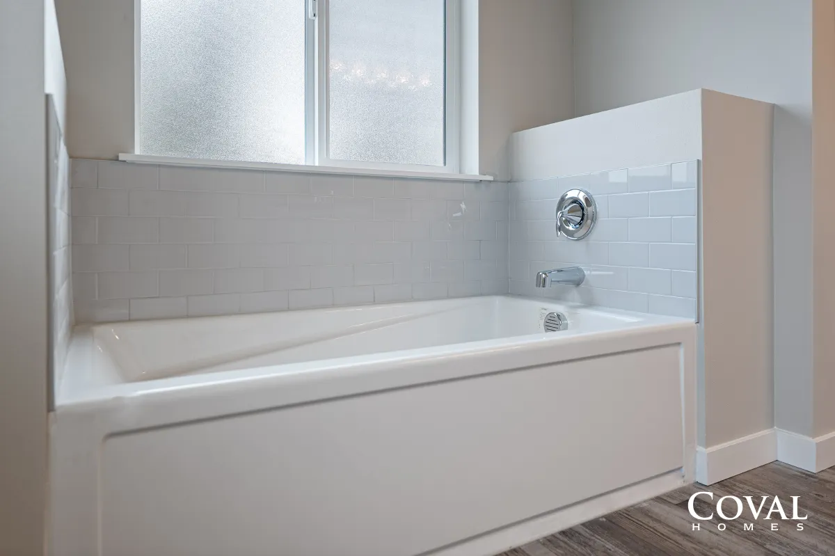 White tiled bathroom with a bathtub, frosted window, and glass shower partition