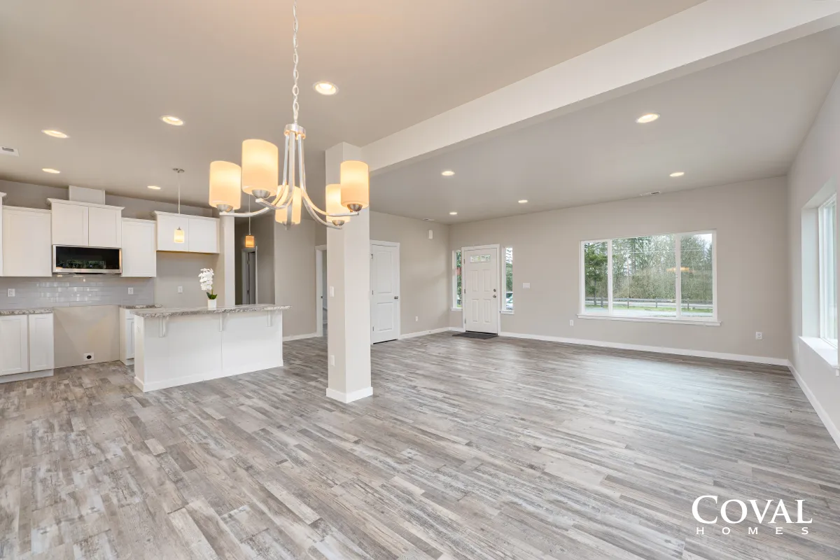 Bright open-plan living room with gray wood floors, white walls, kitchen island, and pendant lights