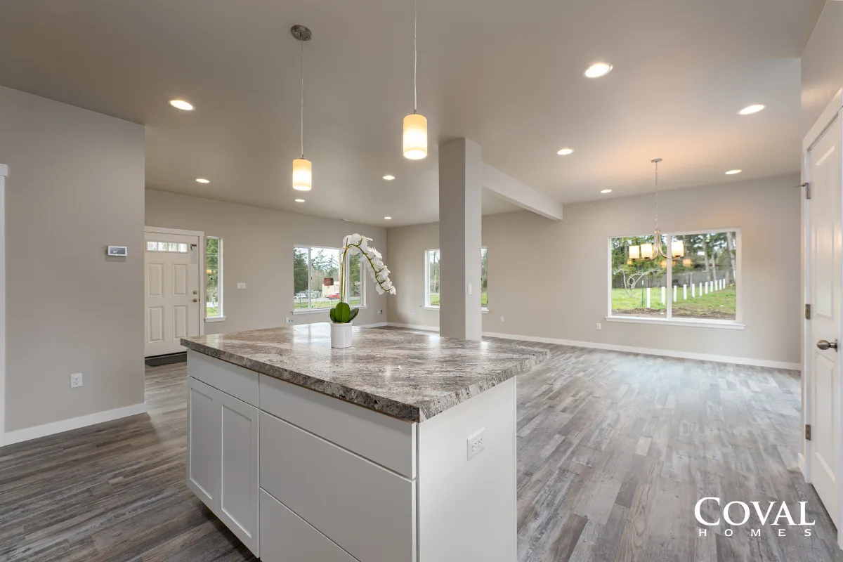 Bright open kitchen and living area with white cabinets, gray wood floors, and large windows