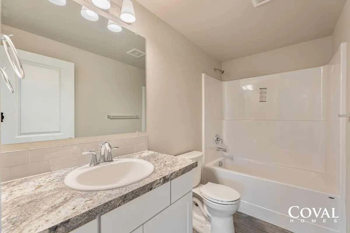Bright bathroom with granite vanity, mirror, sink, toilet, and white tub-shower combo