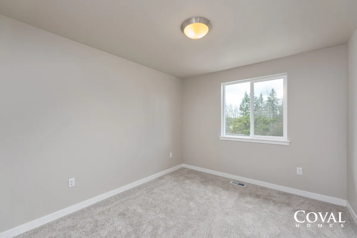 Empty light gray bedroom with carpet, white trim, and a window on the right.