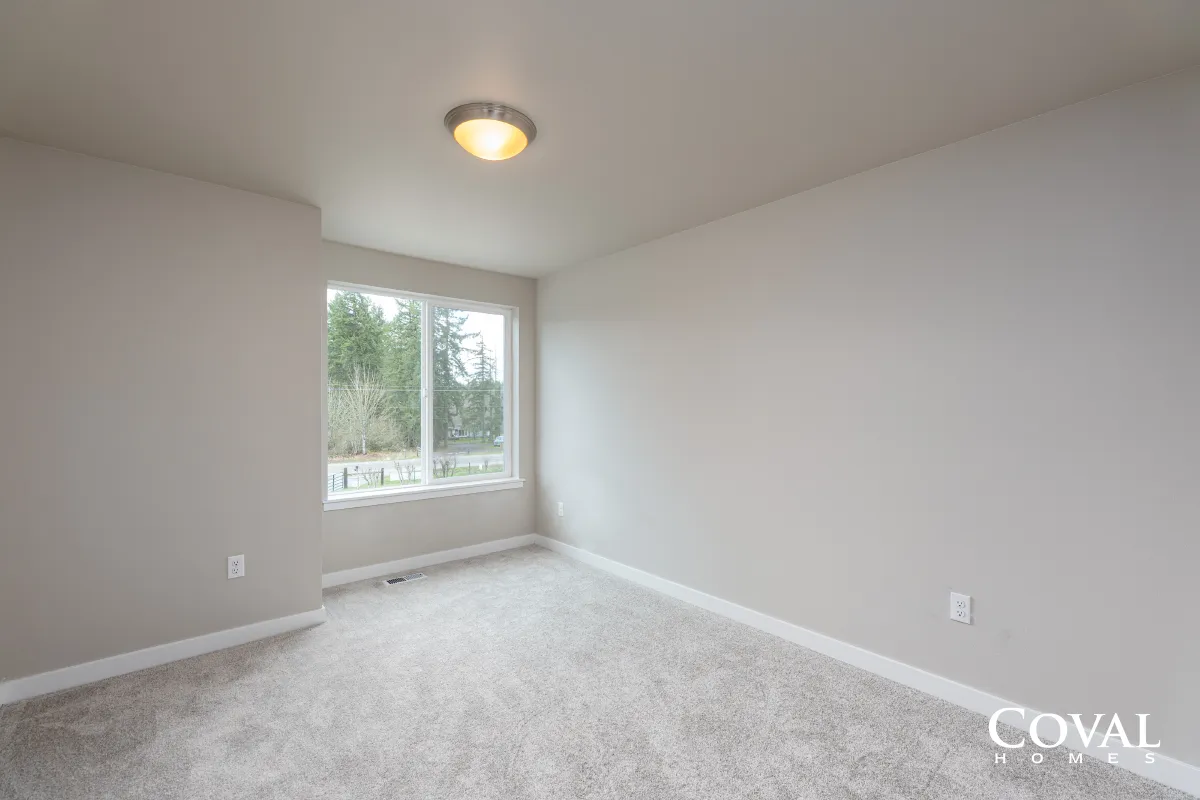 Empty beige bedroom with gray carpet, white walls, a window, and ceiling light.