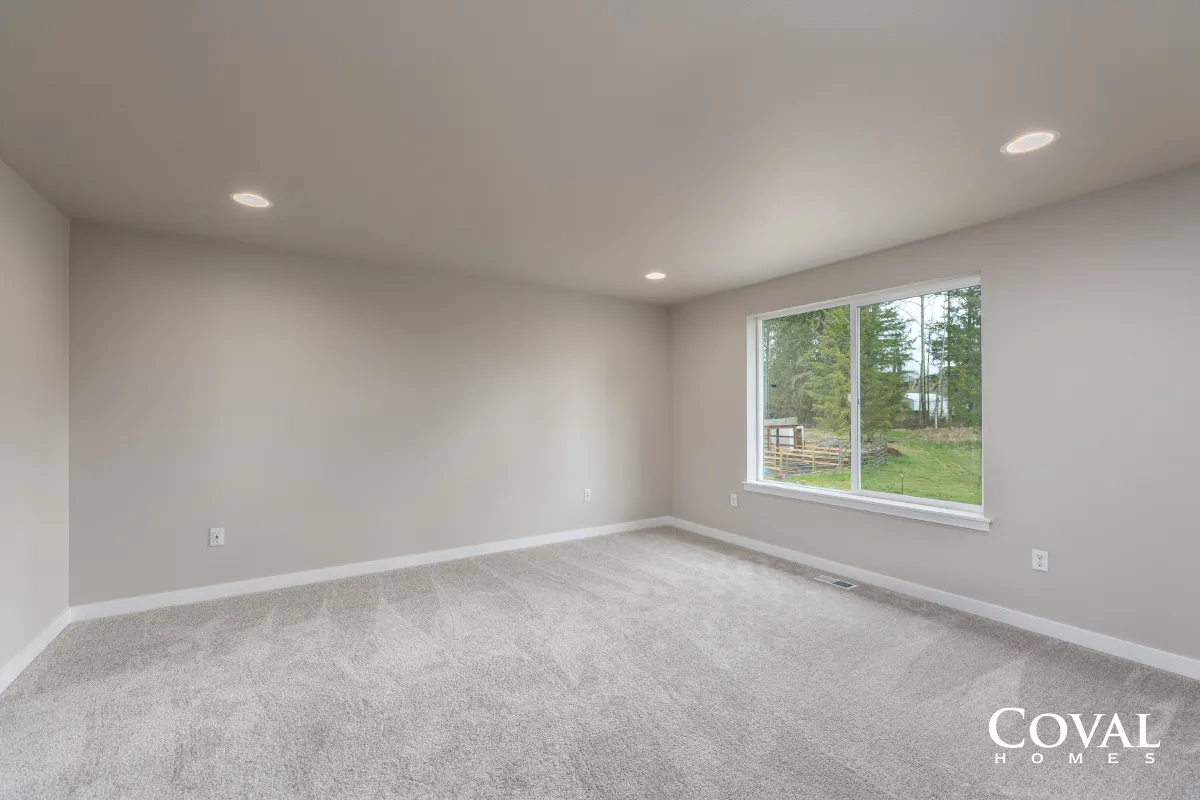 Empty gray-carpeted room with recessed lights and a large window overlooking trees