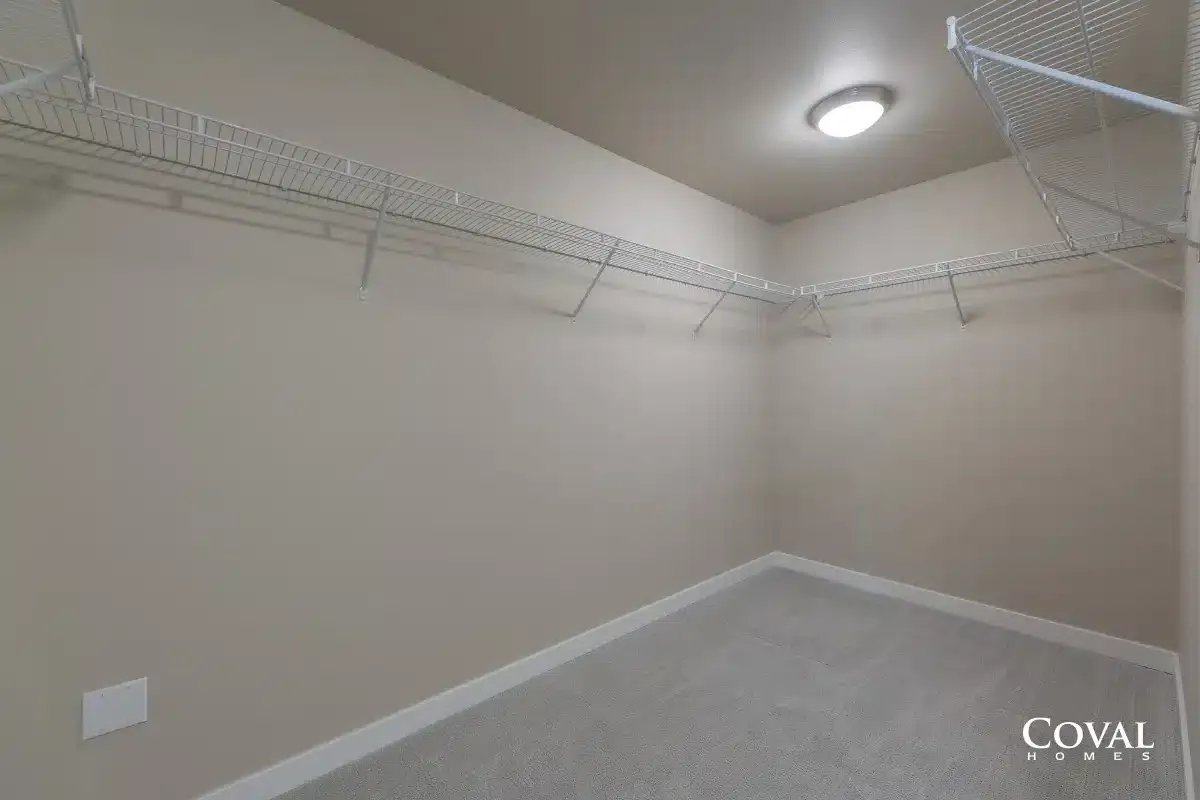 Empty walk-in closet with white wire shelving and beige walls, carpeted floor, and ceiling light.