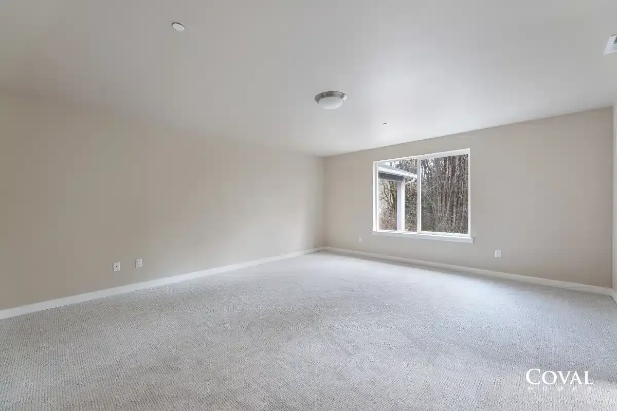 Empty beige carpeted living room with a window and white walls