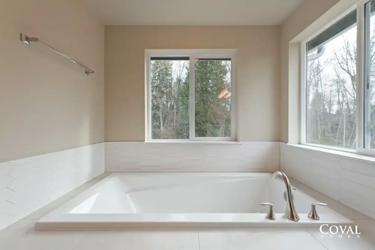 Spacious white bathroom with a large soaking tub and windows overlooking trees.