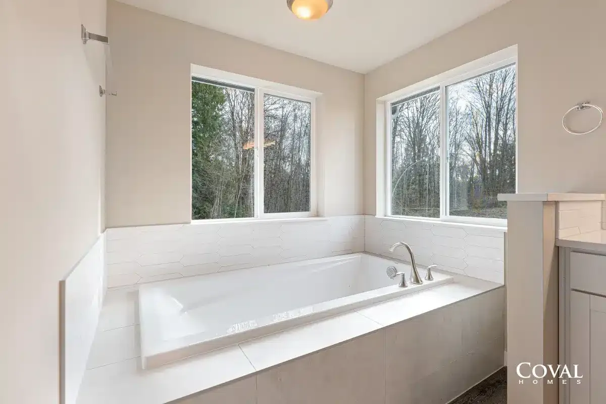 Bright white bathroom with a large soaking tub and windows overlooking trees