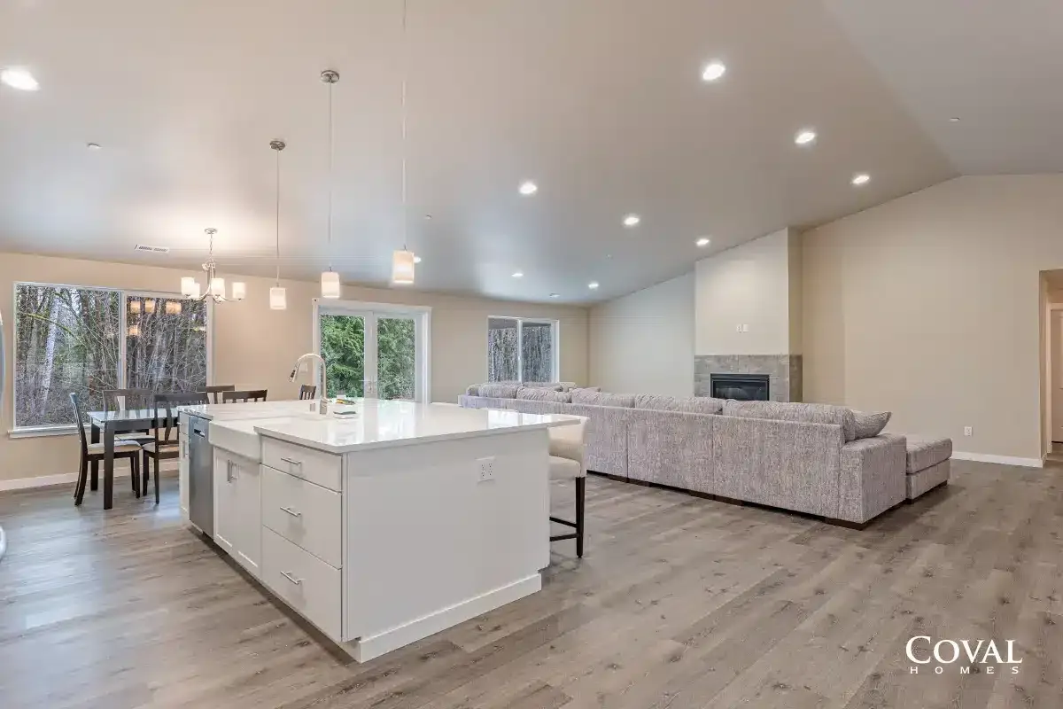 Bright open-concept living room with kitchen island, dining area, gray sofa, and recessed lighting