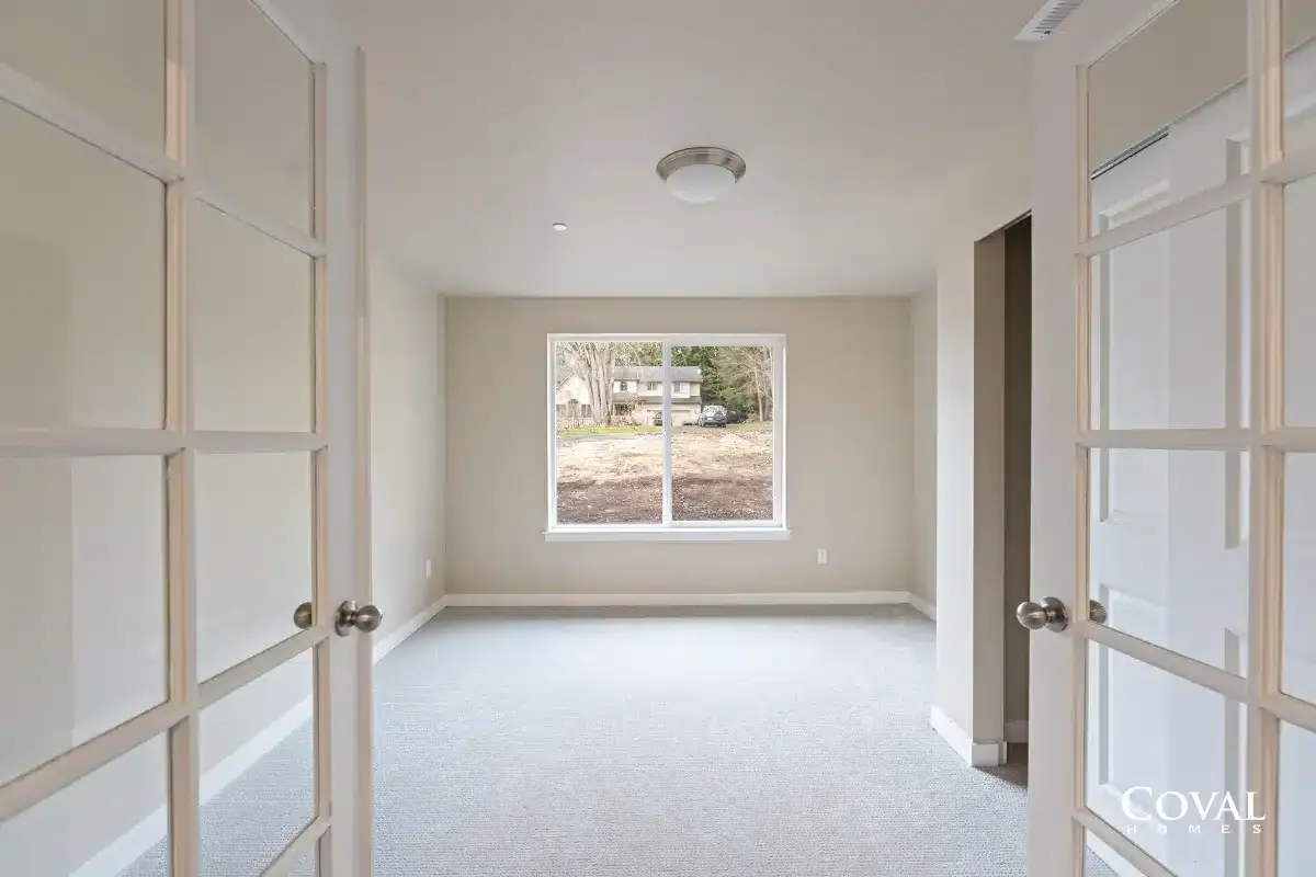 Empty beige room with double doors and a window overlooking trees and a yard