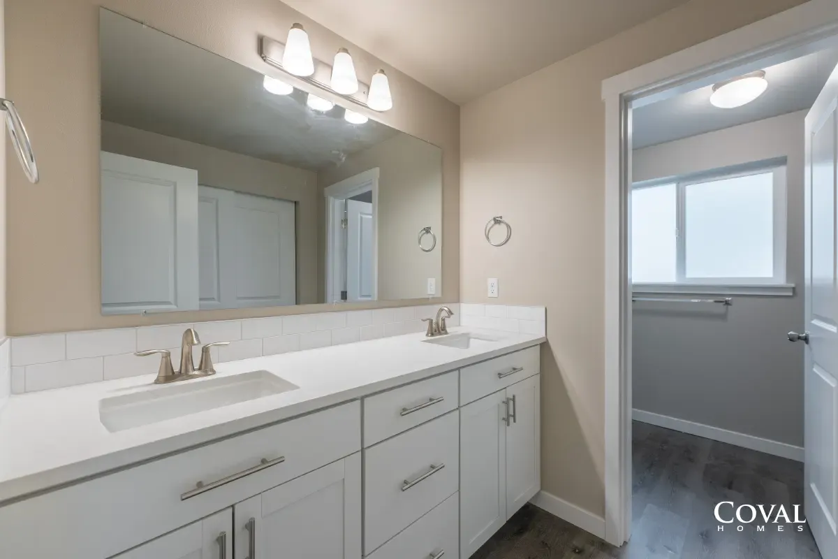 Bright bathroom with white double vanity, large mirror, and tiled floor, viewed toward a small adjoining room