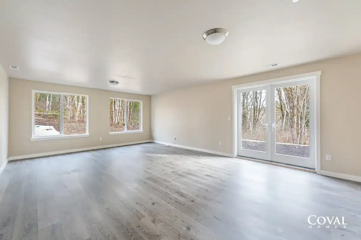 Empty bright living room with light wood floors, neutral walls, and large windows and glass doors.