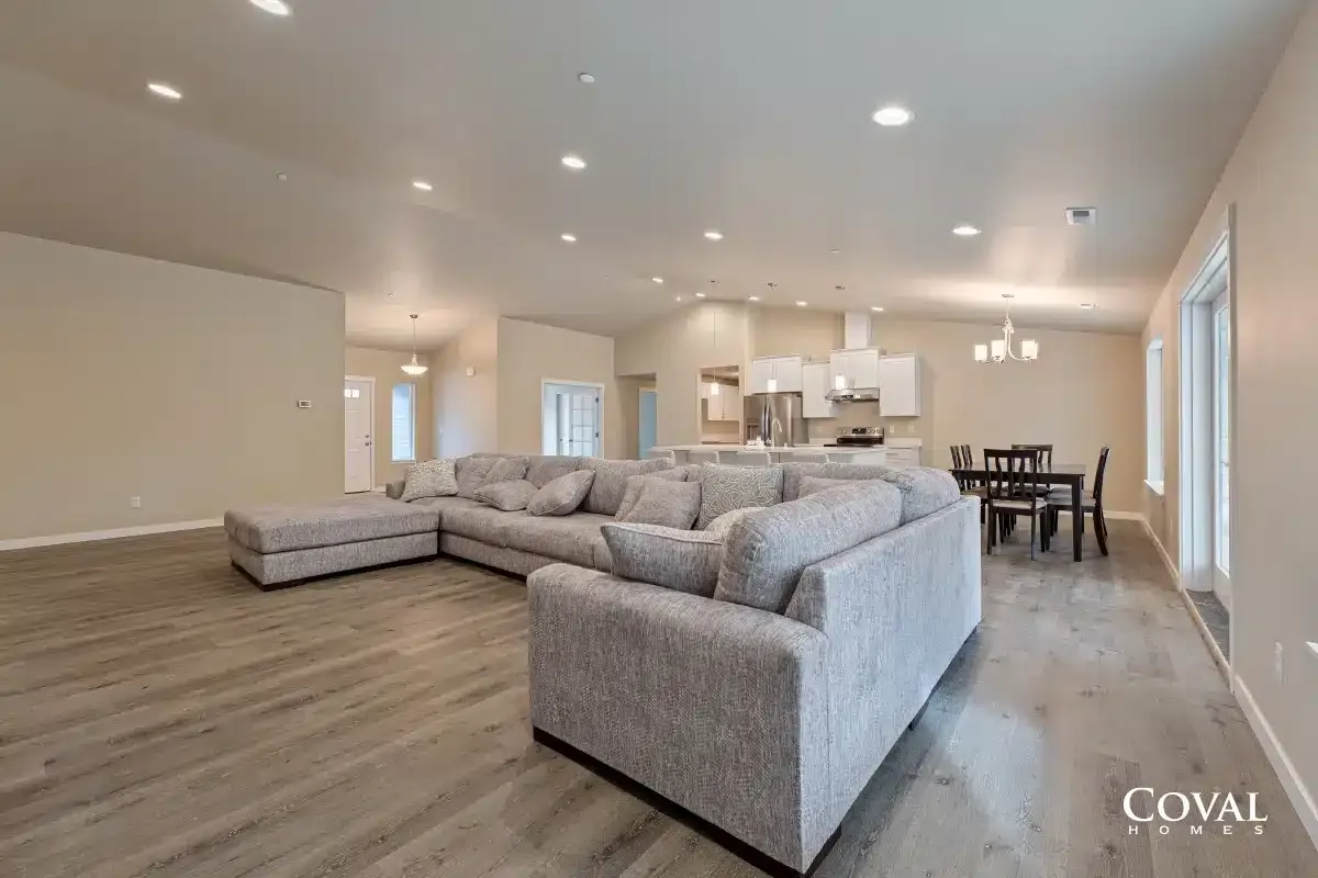 Spacious open-concept living room with gray sectional, wood floors, recessed lights, and dining area.