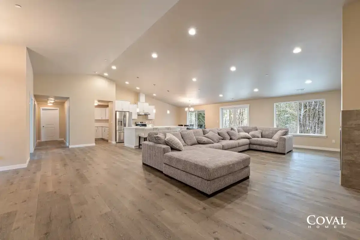 Spacious modern living room with sectional sofa, recessed lights, wood floors, and open kitchen.