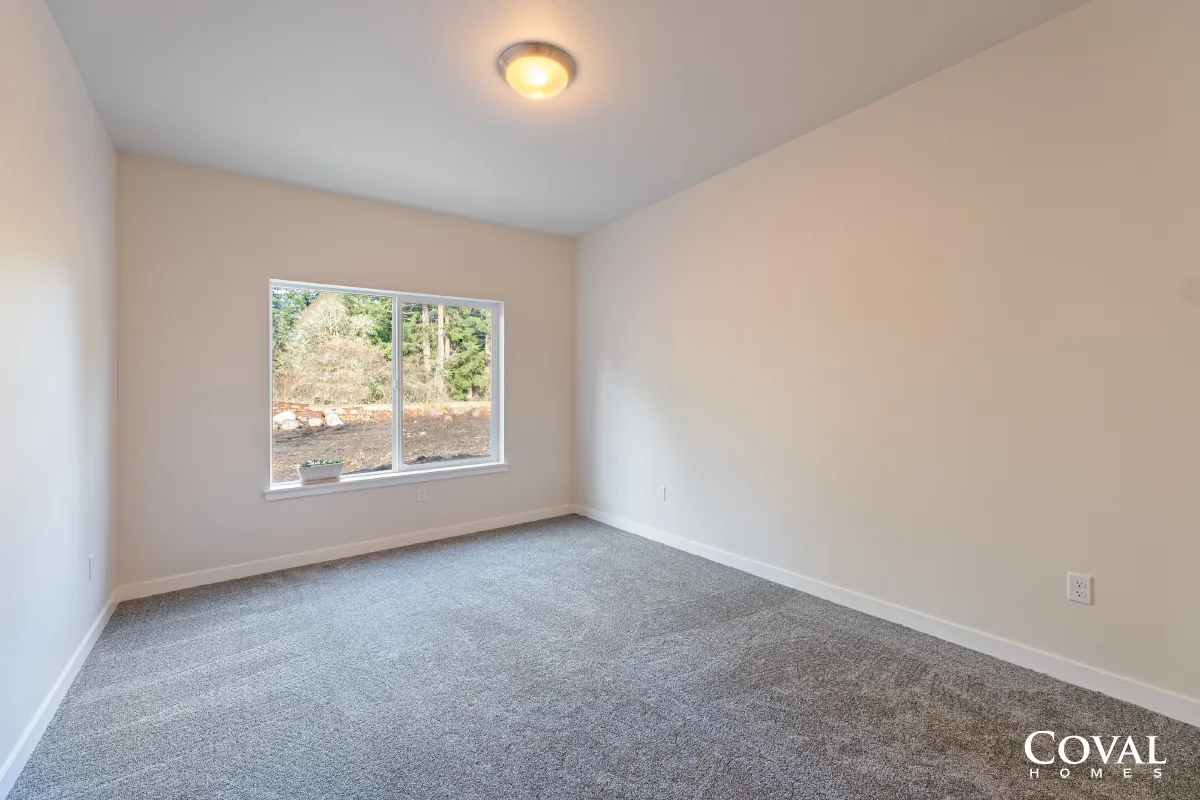 Empty beige bedroom with gray carpet and a window showing trees outside.
