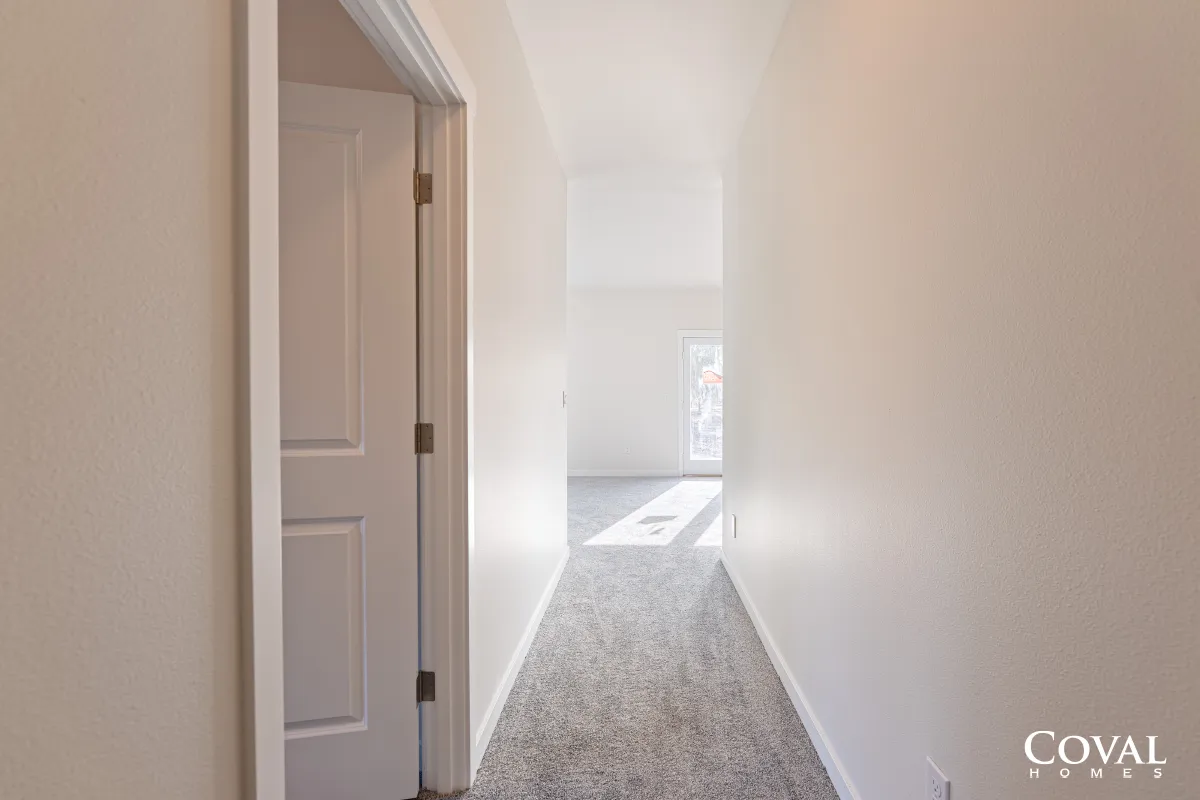 Bright narrow hallway with white walls, open door, and sunlight at the far end