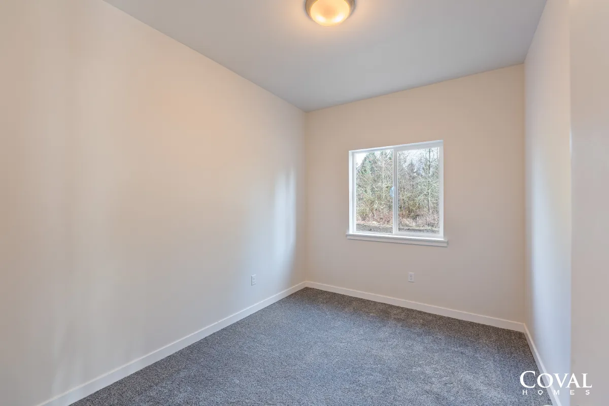 Empty beige bedroom with gray carpet and a window letting in daylight