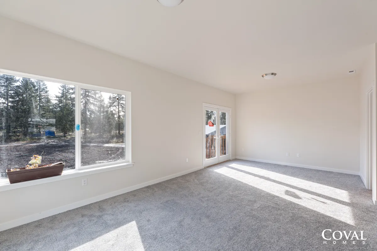 Empty carpeted living room with white walls, large windows, and glass doors letting in bright sunlight