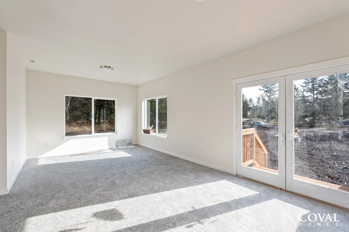 Bright empty living room with gray carpet, white walls, and sliding glass doors to a deck