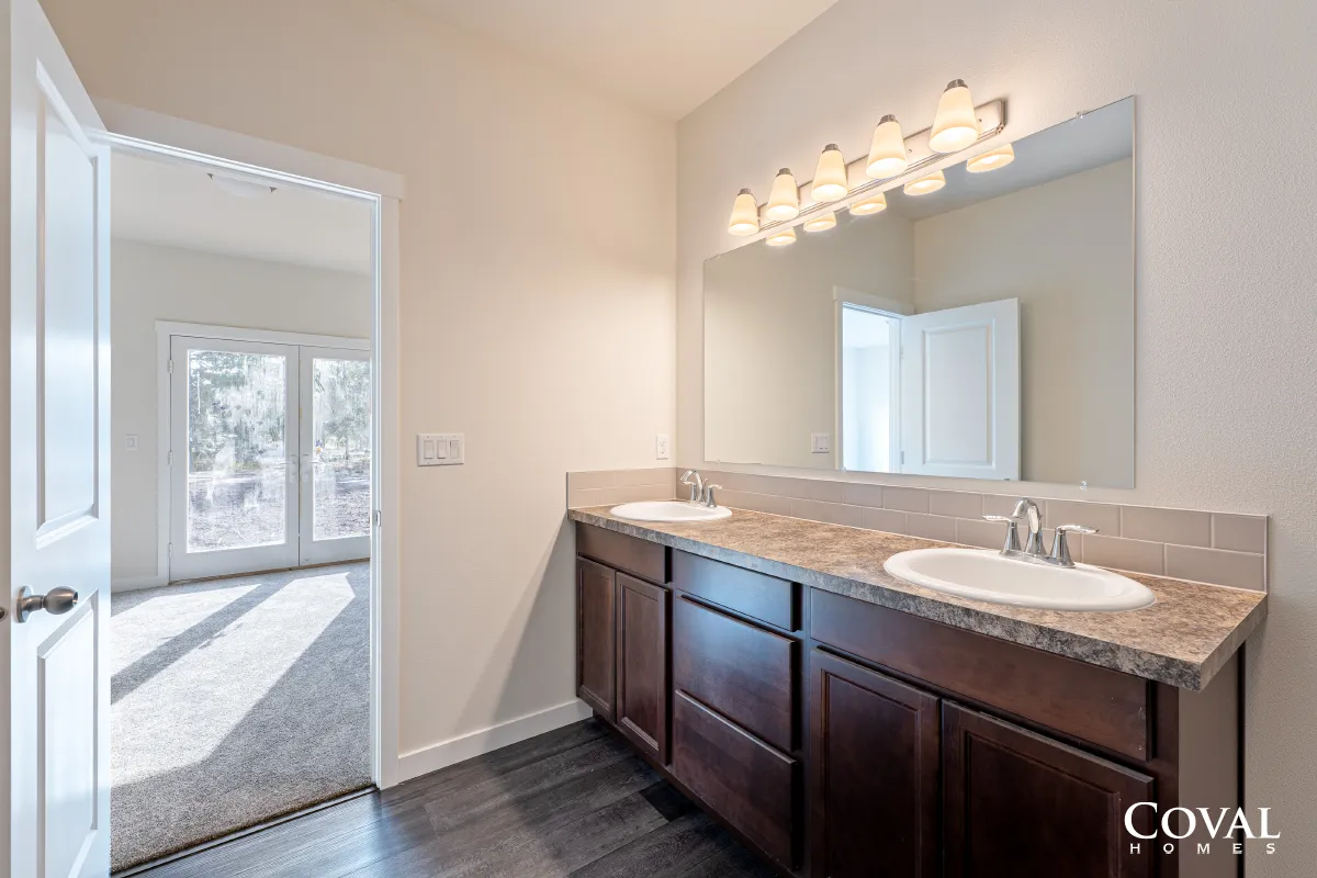 Bathroom vanity with dark wood cabinets, large mirror, and vanity lights beside a bright hallway.
