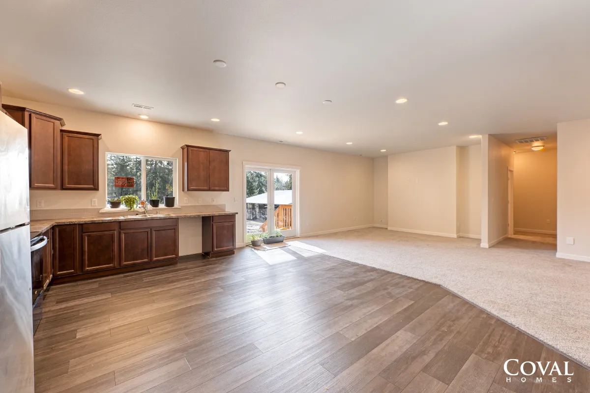 Empty open-plan kitchen and living area with wood floors, dark cabinets, and sliding glass door to patio.