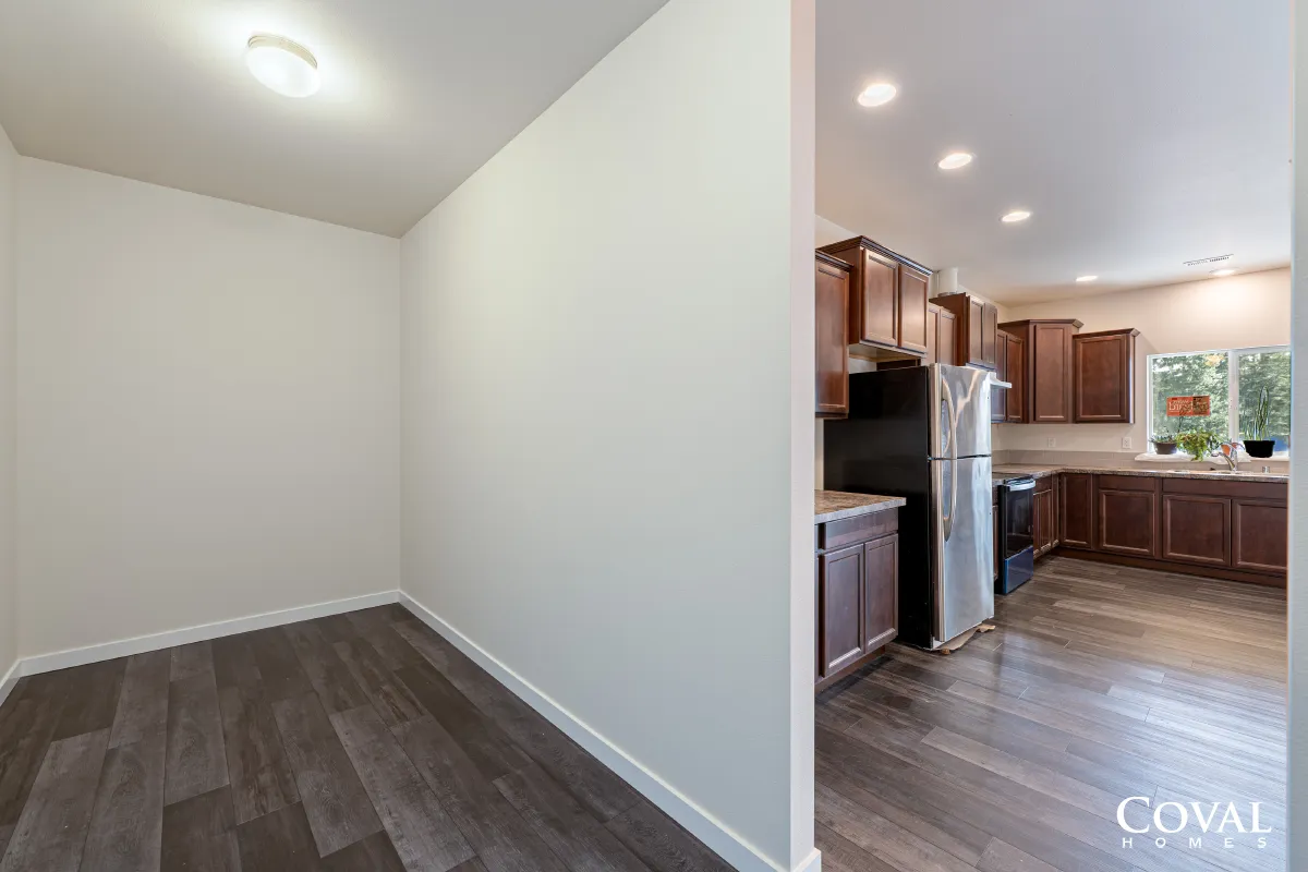 Empty dining area with gray wood floors beside a modern kitchen with stainless steel appliances and dark cabinets