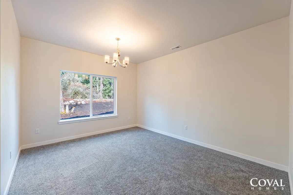 Empty beige carpeted bedroom with a window and chandelier light fixture